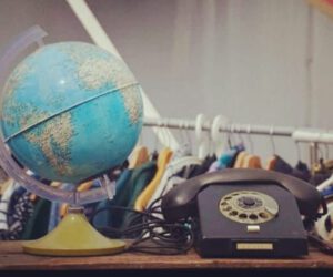 Ein Globus und ein Telefon mit Wählscheibe vor einer gefüllten Kleiderstange.